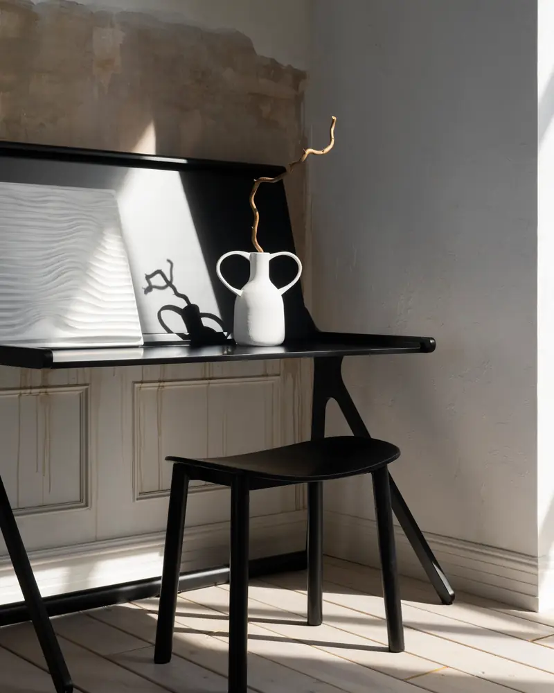 Lo studio: uno scrittoio a ribalta nero con uno sgabello, la luce del mattino che entra dalla finestra